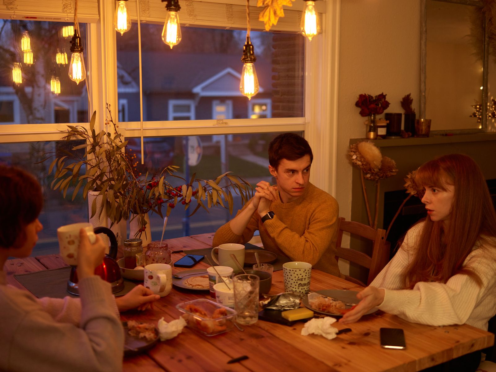Three people talking around a dining table with mugs
