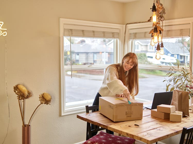 A Woman Unboxing A Package On A Wooden Table