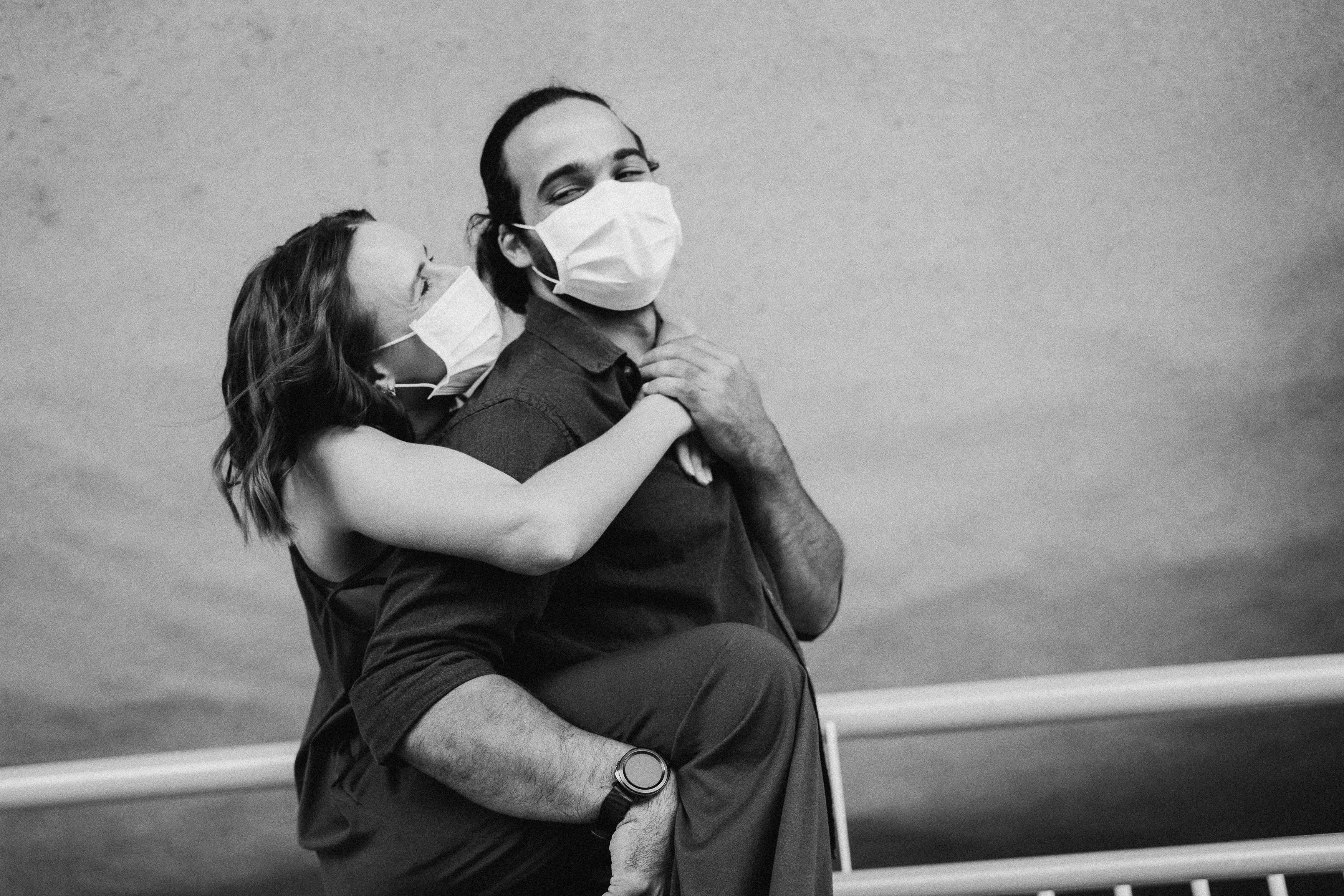 A couple wearing face masks share a tender embrace, capturing love in challenging times.