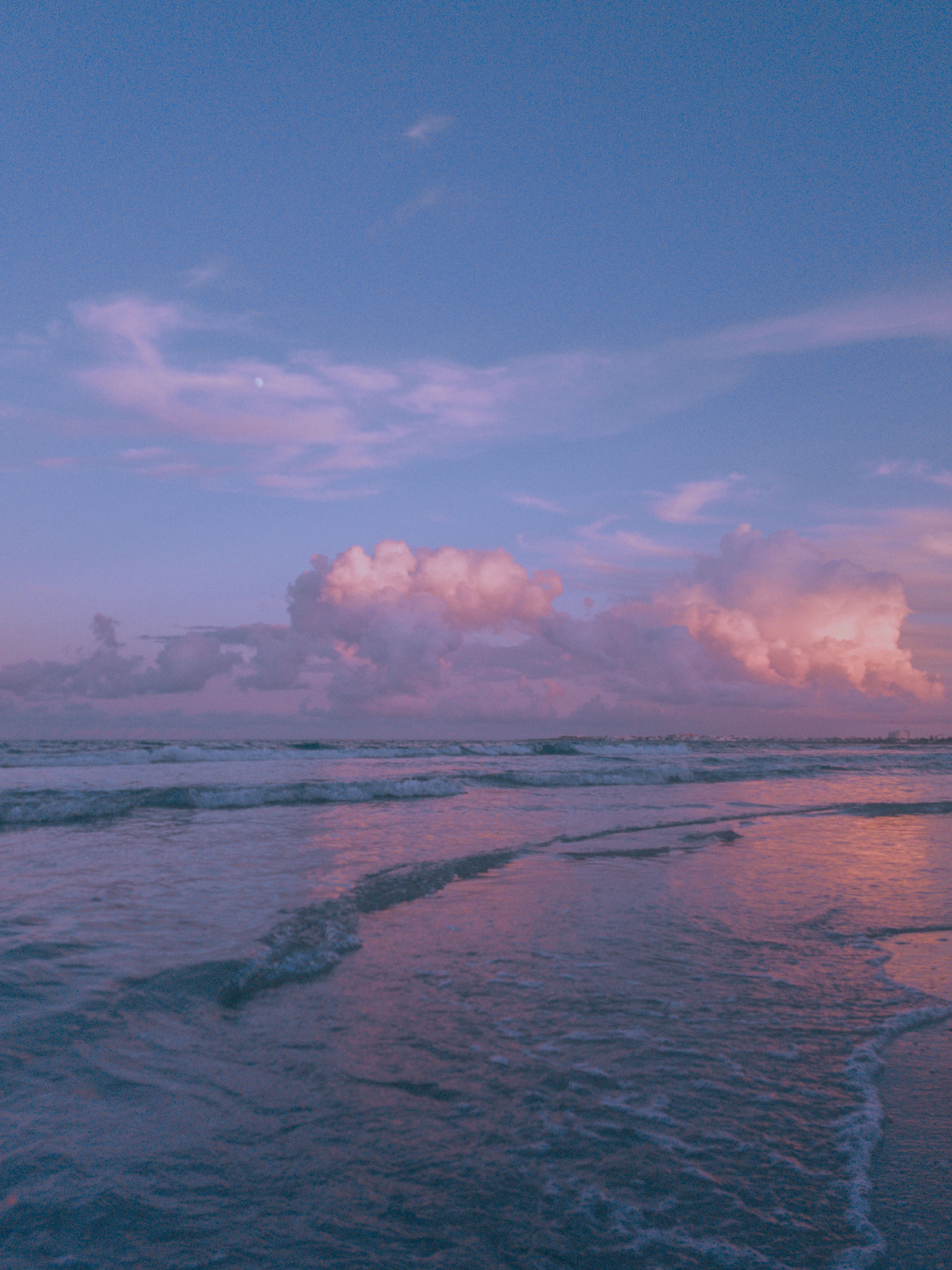 Capture the tranquility of a beach at sunrise with soft pink clouds and gentle waves.