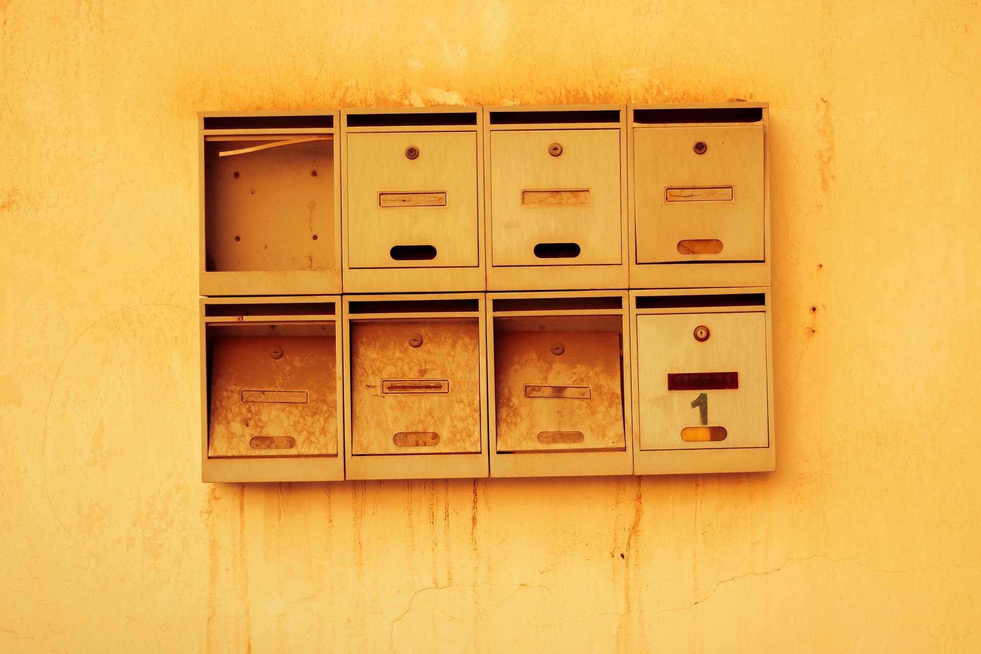 Old metal mailboxes attached to a textured wall with a warm vintage tone.