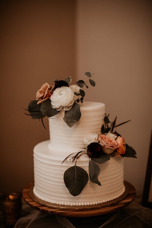 A White Wedding Cake Decorated with Flowers and Leaves on a Cake Stand
