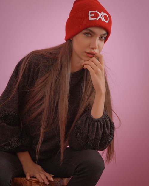 Free Stylish woman in a red beanie poses against a pink background in a studio setting. Stock Photo