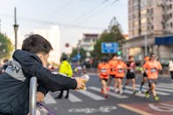 A Child in Black Jacket Leaning on a Steel Barrier Watching a Race