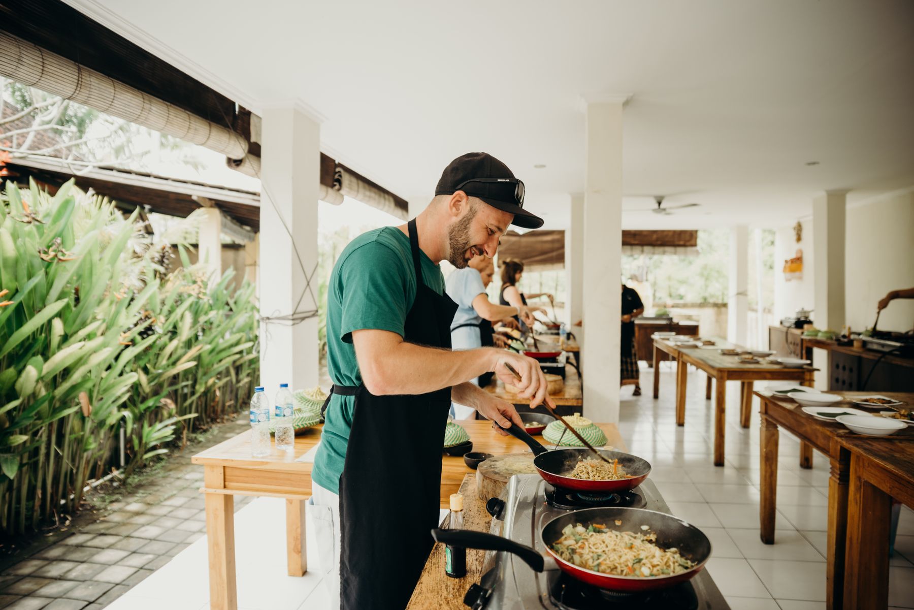 Cook preparing food in an open-air Balinese kitchen surrounded by tropical plants