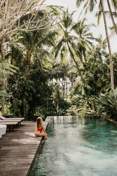 Woman relaxing by a tropical poolside with lush palm trees in Bali, Indonesia.