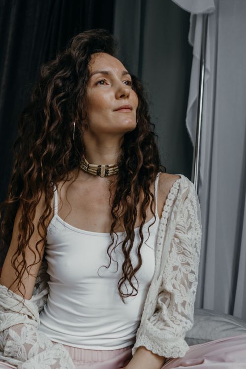 Free Portrait of a pensive woman with curly hair, dressed in a white top and lace cardigan, sitting indoors. Stock Photo