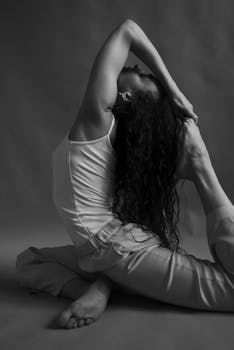Black and white portrait of a woman performing a yoga pose in a studio, emphasizing flexibility and elegance.