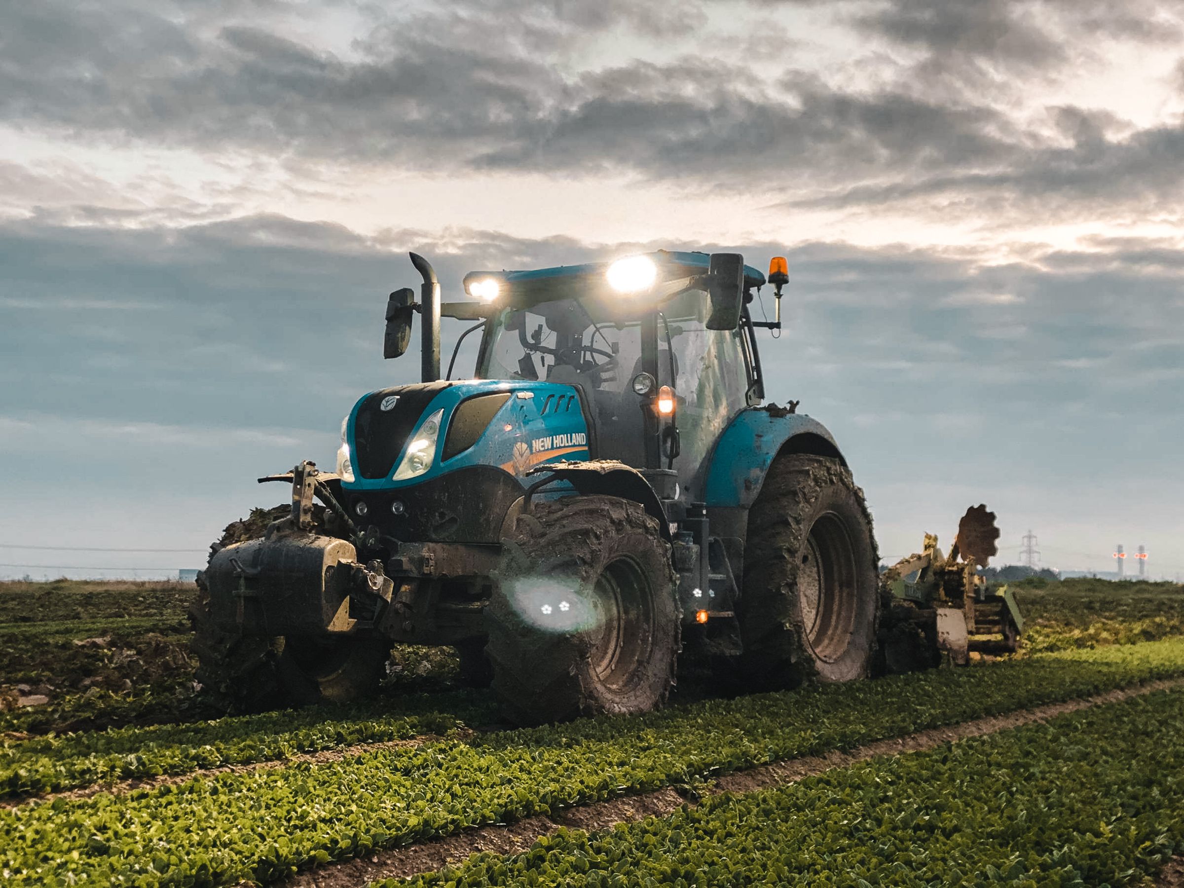 Tractor working a field at dusk with its work lights on