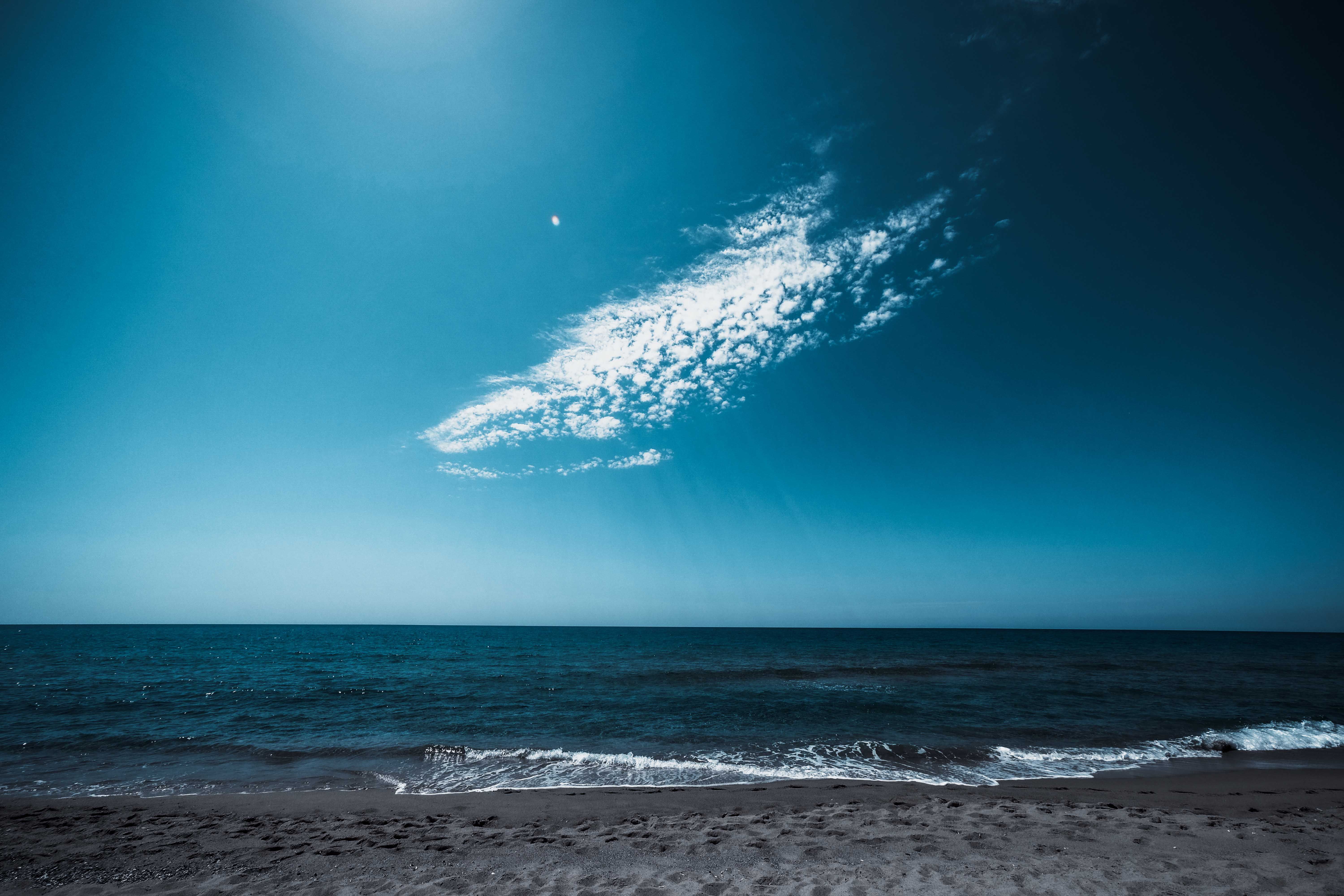 Scenery view of endless blue sea with foamy waves rolling on sandy shore under bright sky