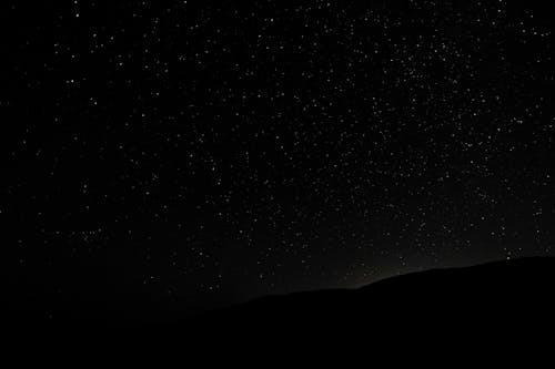 Dark endless sky covered with shining luminous stars above silhouette of hill at night