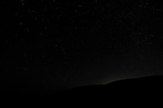 Dark endless sky covered with shining luminous stars above silhouette of hill at night