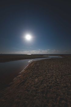 Scenery of bright sun on blue sky shining over narrow river flowing through sandy terrain