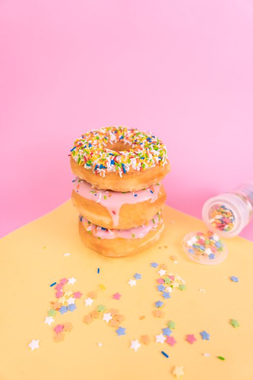 Free Stacked doughnuts with colorful sprinkles on pink background, perfect for dessert themes. Stock Photo
