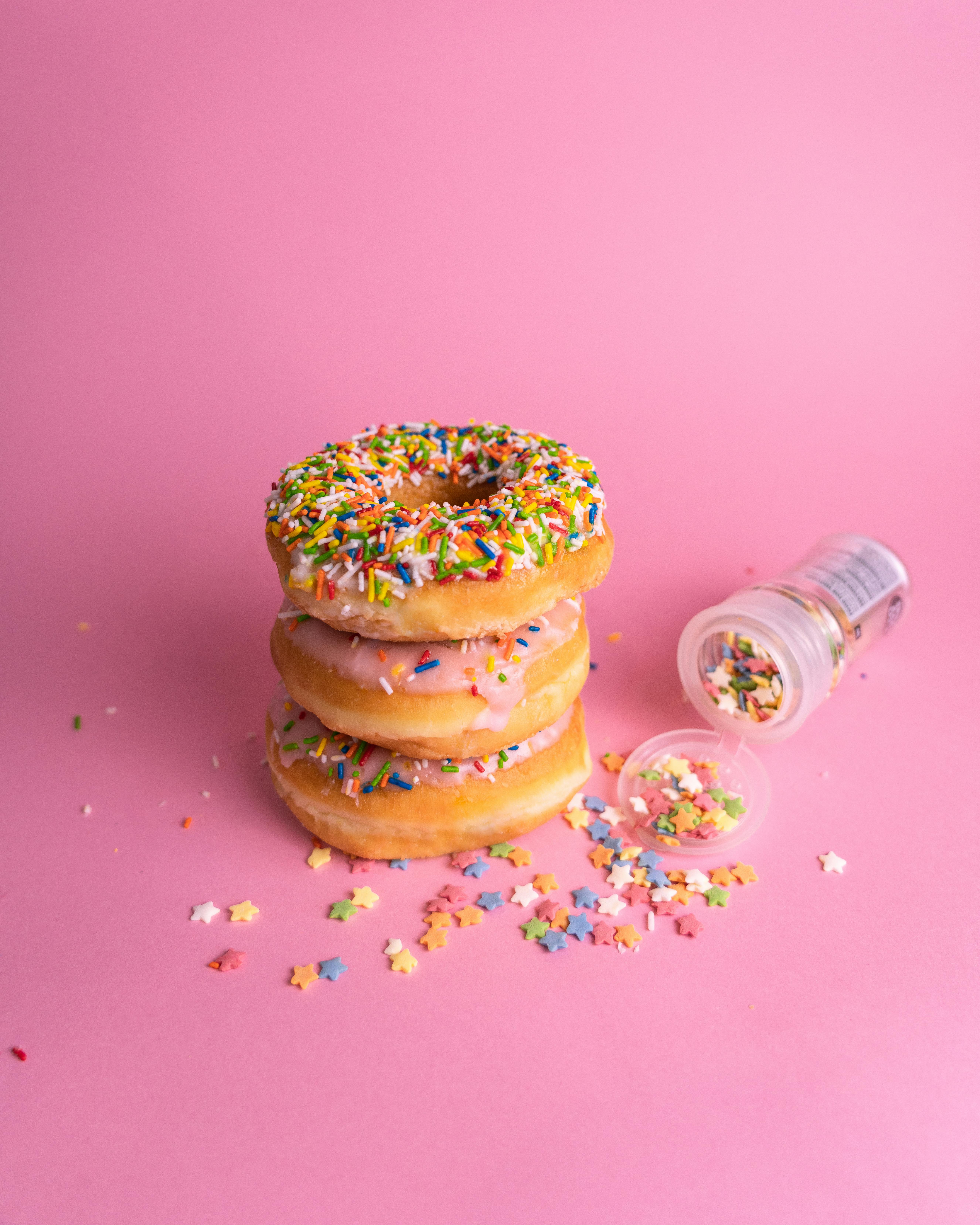 A stack of delicious donuts topped with rainbow sprinkles on a pink backdrop, perfect for food photography enthusiasts.