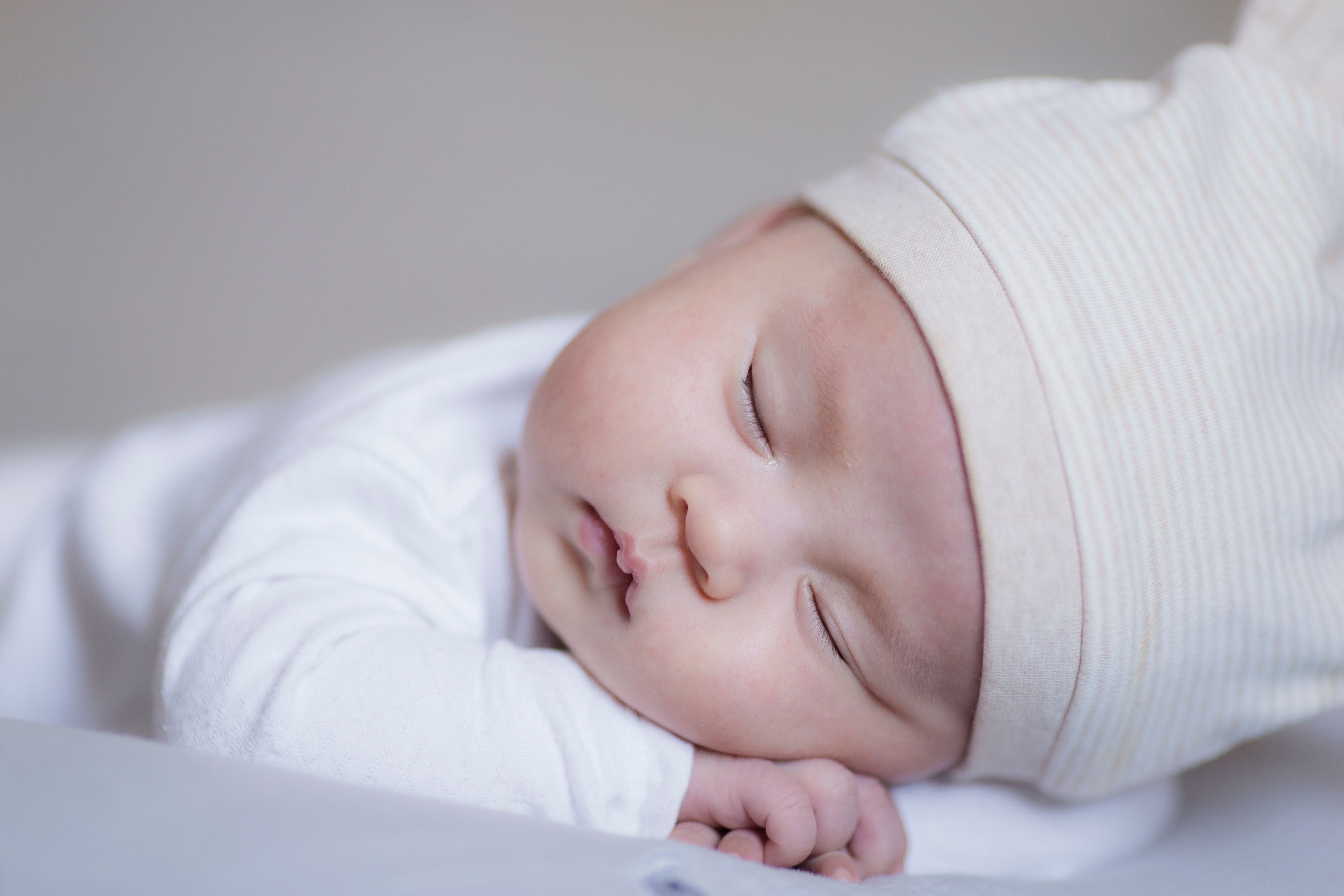 Close-up of a peaceful baby sleeping in a cozy white outfit and hat, showcasing innocence and serenity.