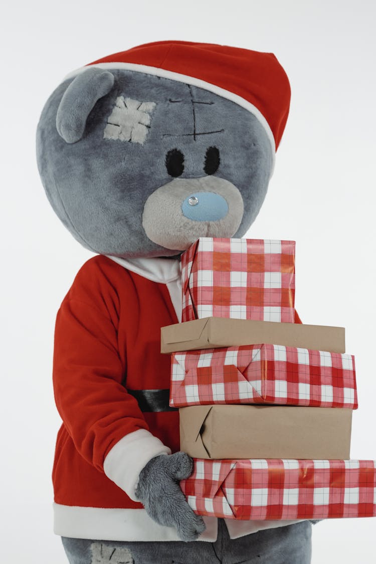 A Teddy Bear Mascot In Santa Claus Costume Holding Christmas Presents