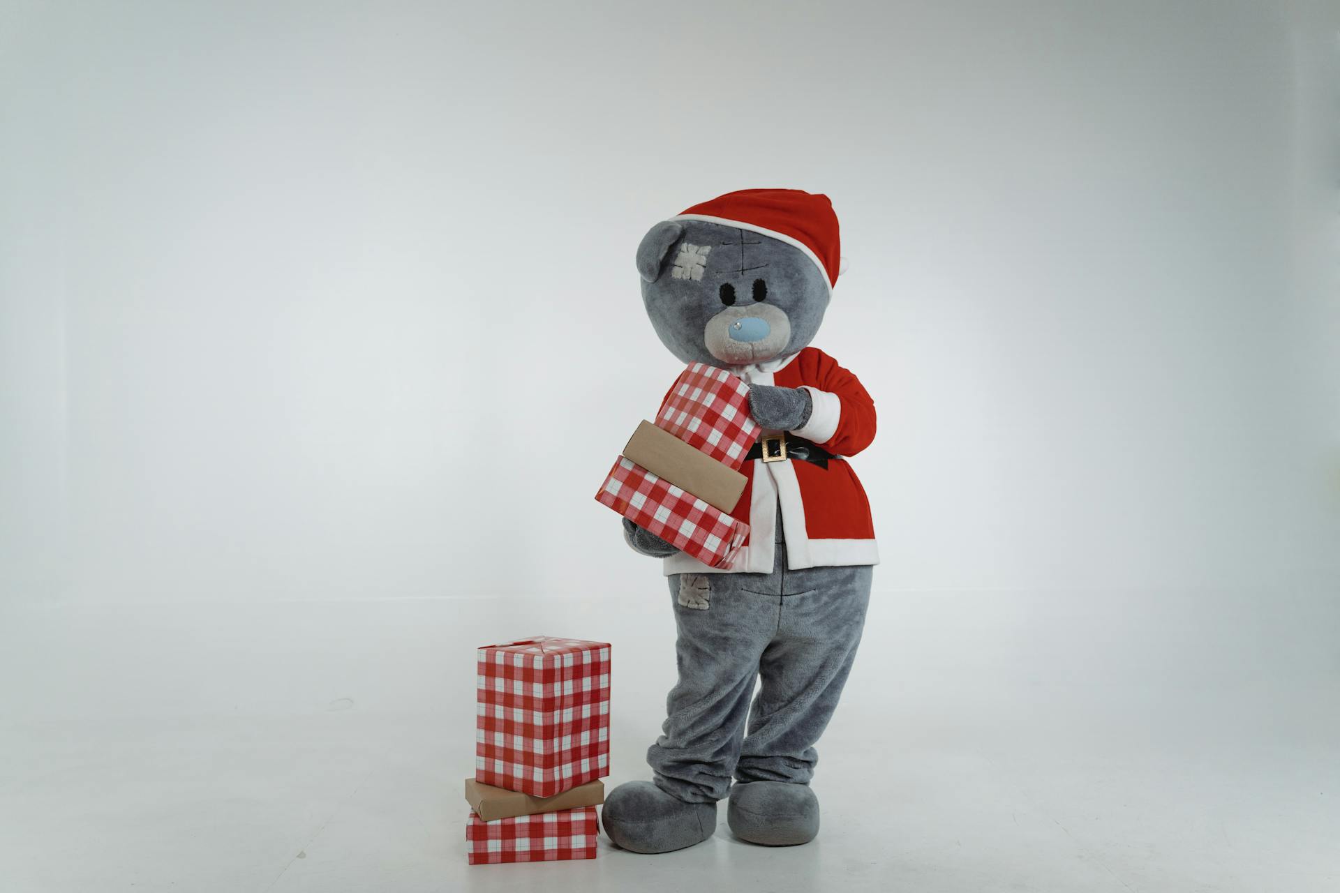 A Teddy Bear Mascot in Santa Claus Costume Holding Christmas Presents