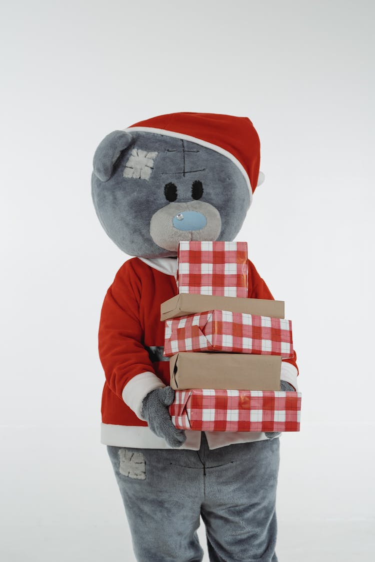 A Teddy Bear Mascot In Santa Claus Costume Holding Christmas Presents