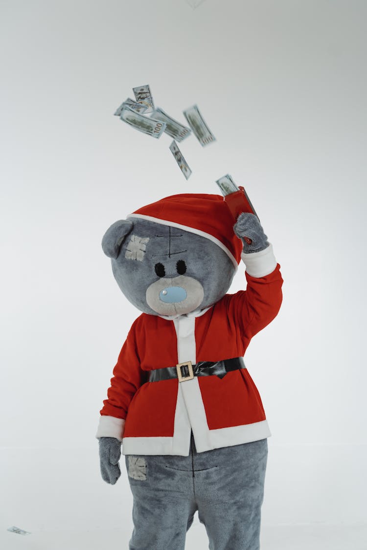 A Teddy Bear Mascot In Santa Claus Costume Using A Money Gun