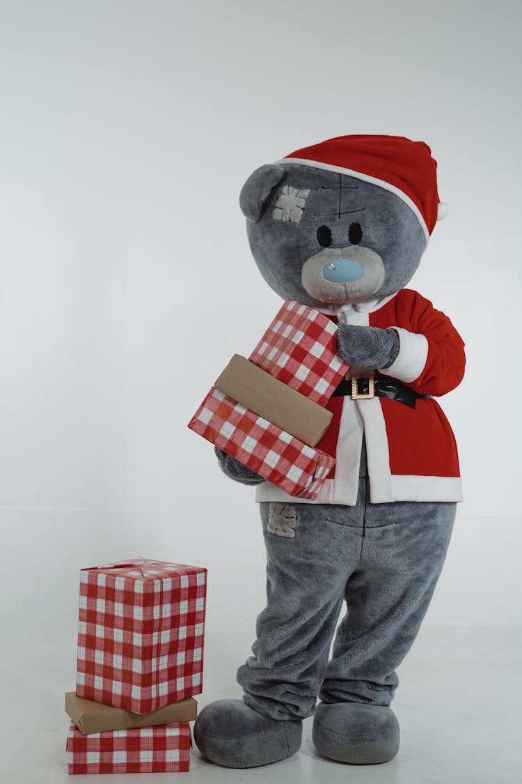 A Teddy Bear Mascot In Santa Claus Costume Holding Christmas Presents