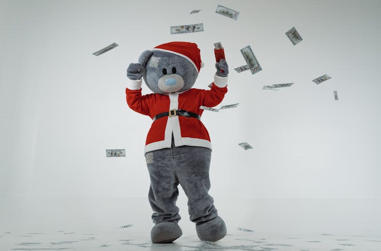 A Teddy Bear Mascot In Santa Claus Costume Using A Money Gun