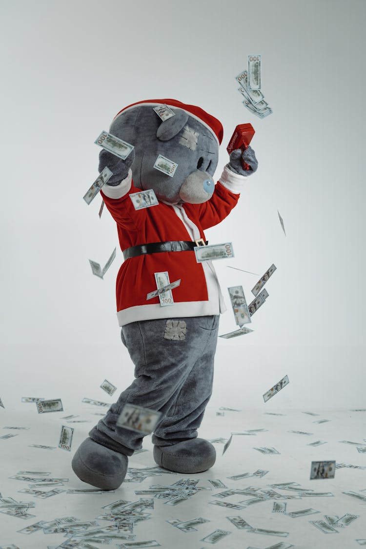 A Teddy Bear Mascot In Santa Claus Costume Using A Money Gun