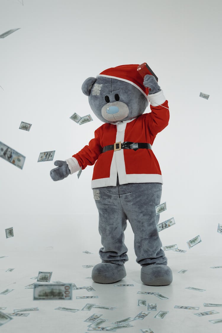 A Teddy Bear Mascot In Santa Claus Costume Using A Money Gun