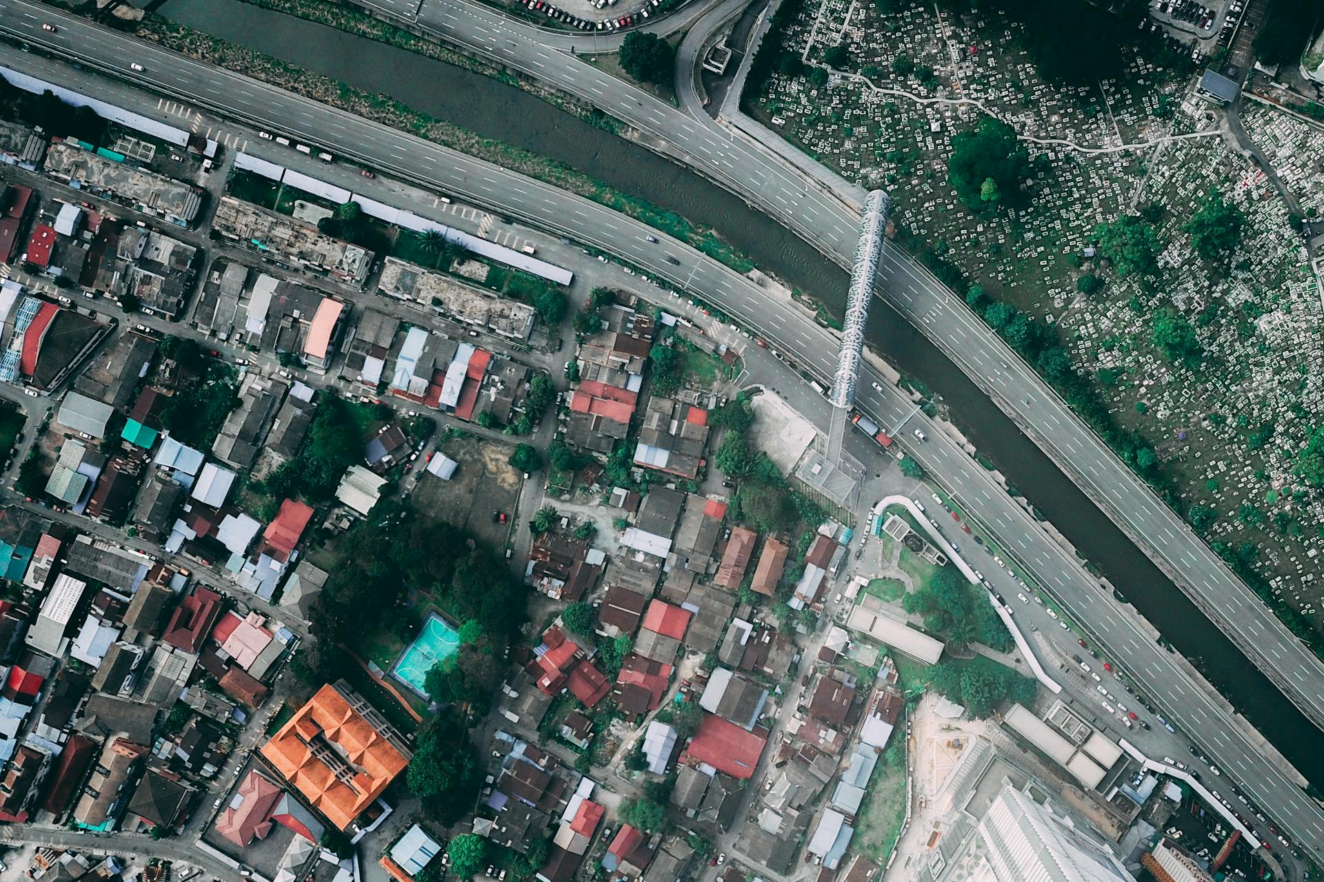 Aerial view of modern city with various residential buildings located on bank of narrow river surrounded by asphalt roadway and glass footbridge