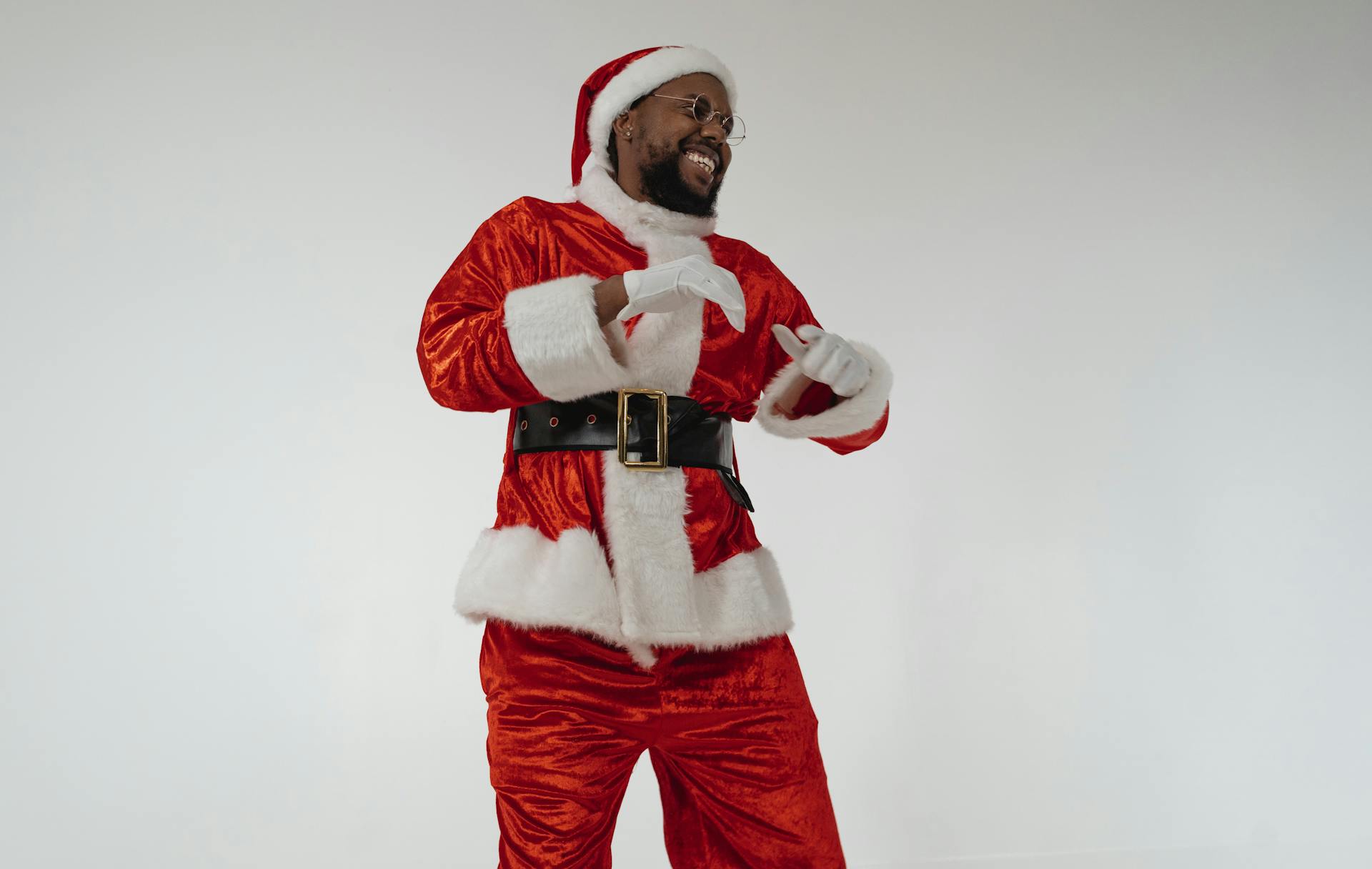 A cheerful man in a Santa Claus costume dancing with a smile in a studio setting.