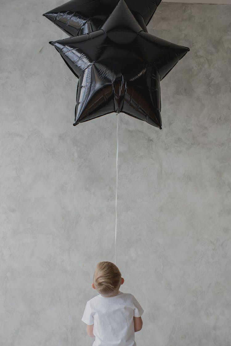 Child Looking At A Black Star Shaped Balloons 