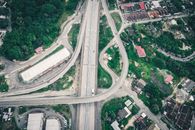 Aerial view of asphalt roadway running among industrial building and residential houses located in suburb area surrounded with green trees