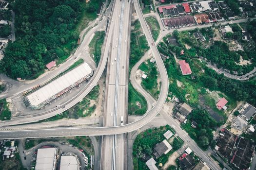 Aerial view of asphalt roadway running among industrial building and residential houses located in suburb area surrounded with green trees