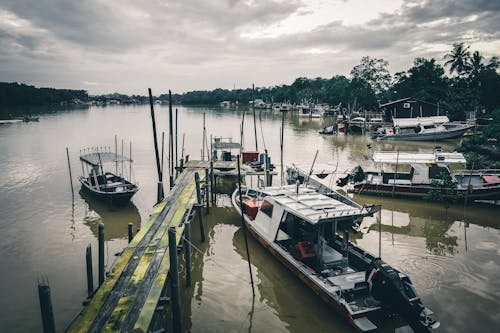 Rippling muddy sea surrounded by old wooden pier with fishing motorboats and yachts located in tropical area on cloudy day