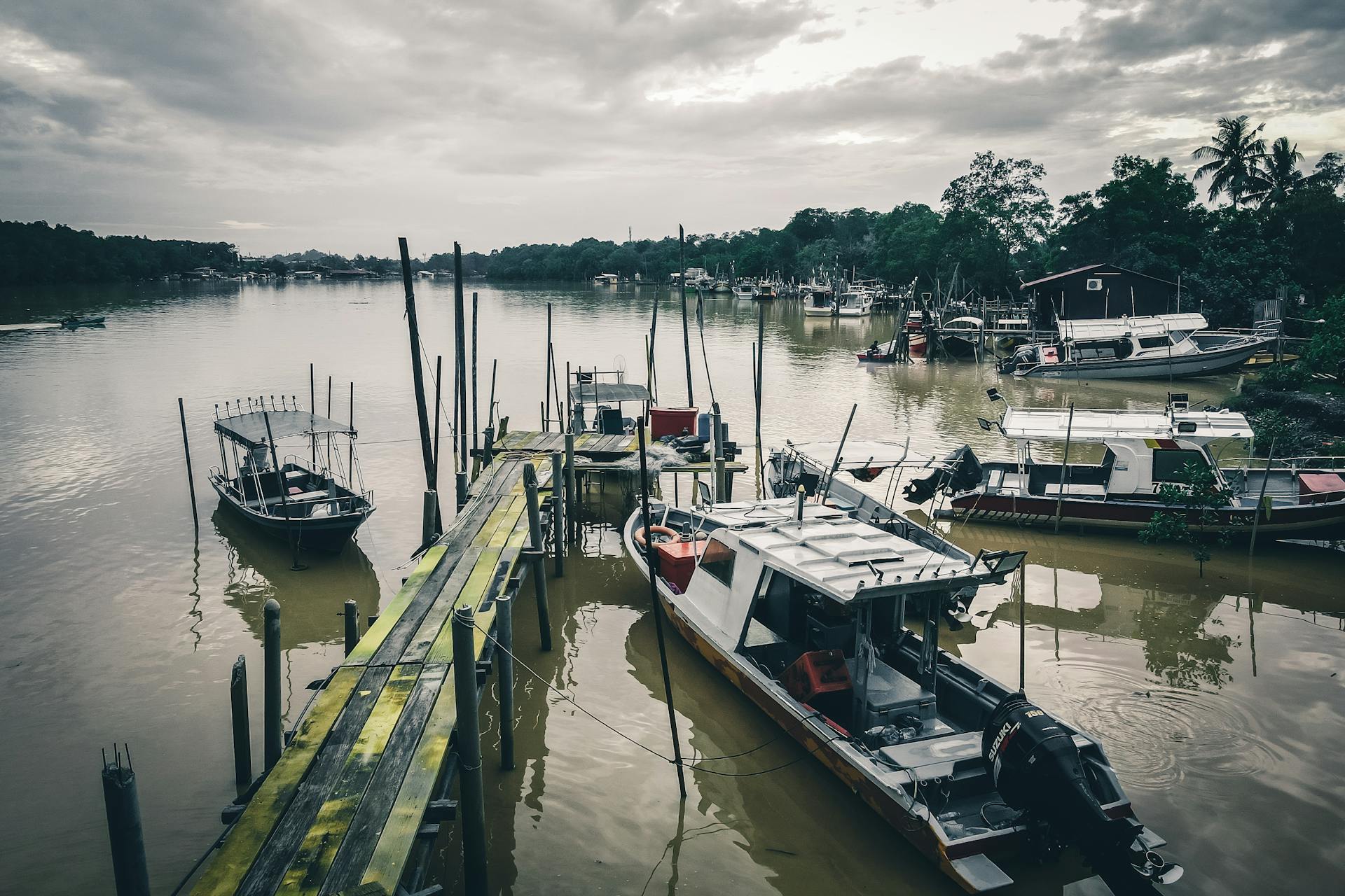 Rippling muddy sea surrounded by old wooden pier with fishing motorboats and yachts located in tropical area on cloudy day