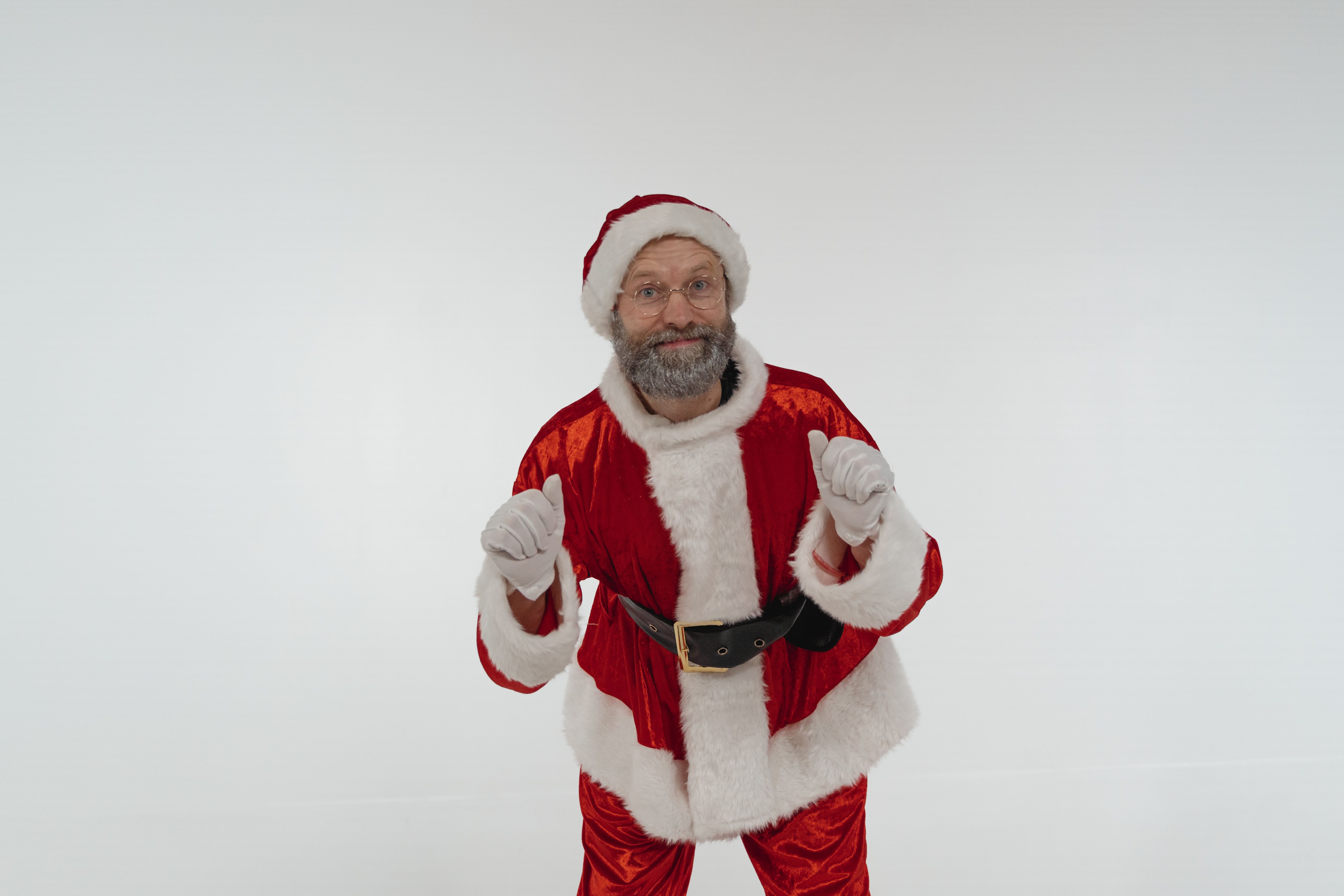 Smiling elderly man in Santa costume posing indoors with cheerful expression.