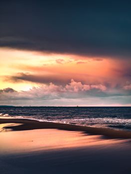A serene view of the sunset over the tranquil beach in Gdańsk, Poland, with vibrant skies and gentle waves.