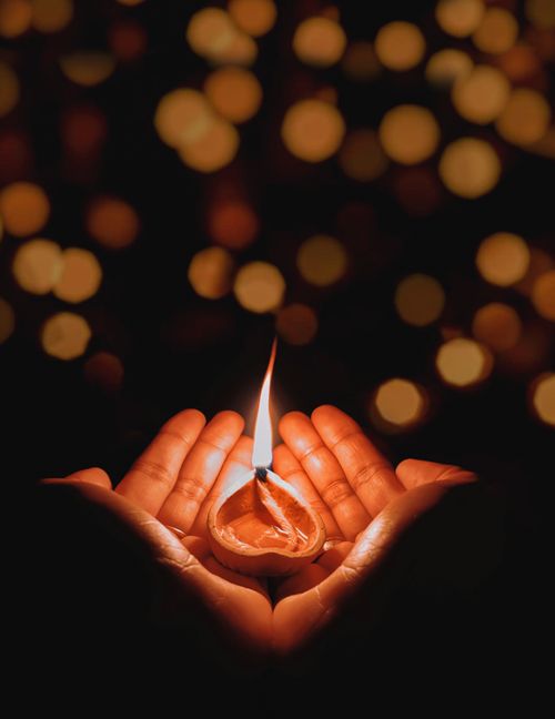 Free A pair of hands holding a lit candle against a bokeh background, evoking warmth and peace. Stock Photo