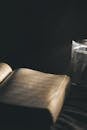 An Open Book Beside a Clear Glass on a Black Surface