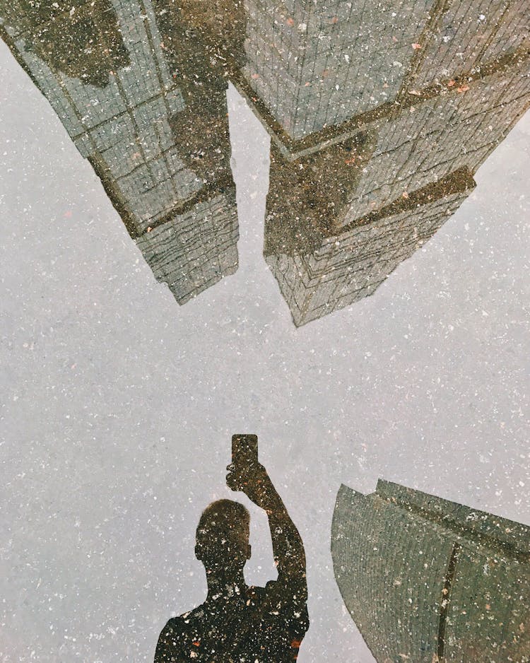 A Reflection Of A Man Taking A Selfie On A Puddle Under The Snow