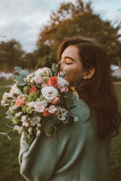 Free A woman in a green sweater enjoys a colorful bouquet of flowers in an outdoor setting. Stock Photo