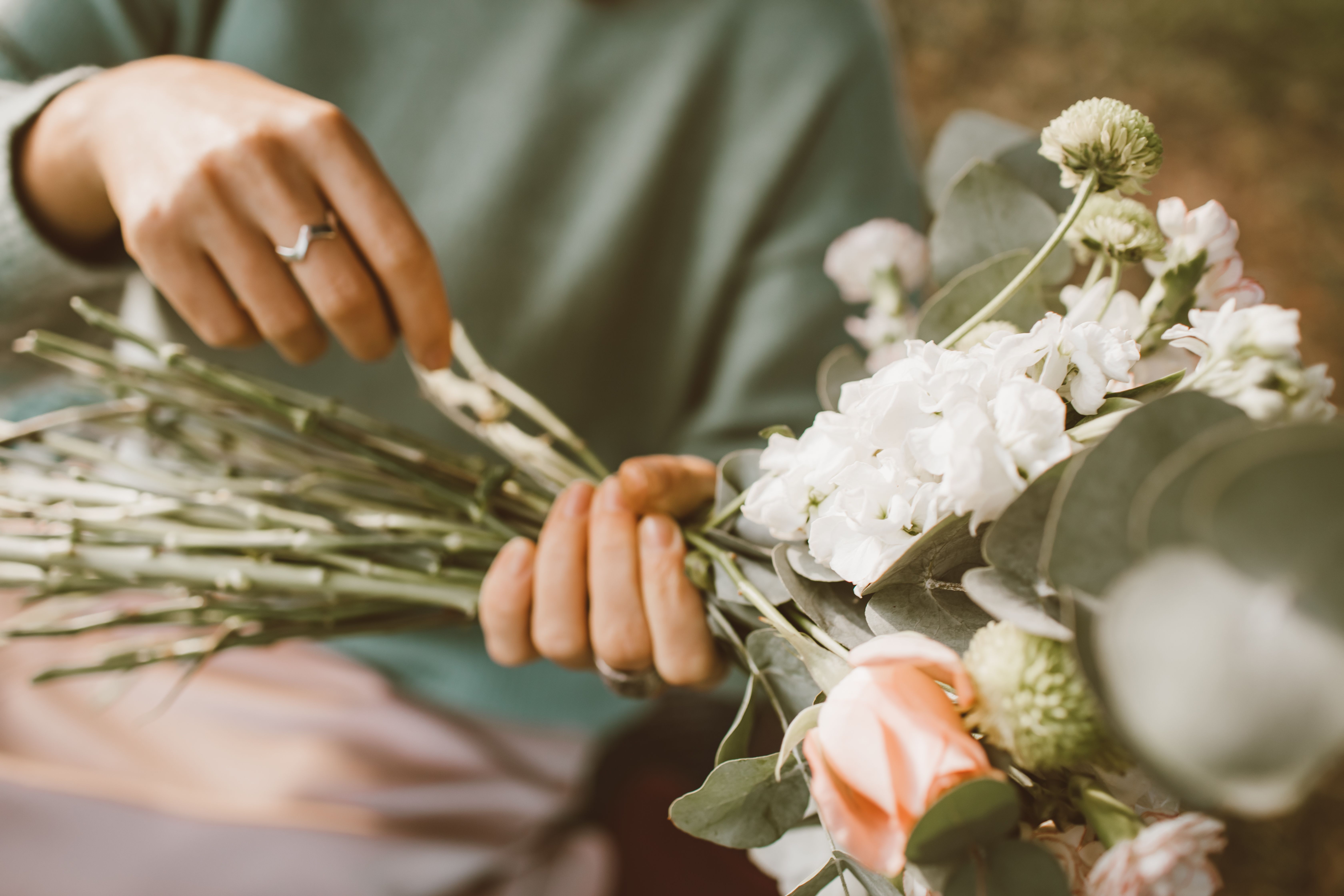 An artistic close-up of hands styling a beautiful bouquet with roses and greenery.