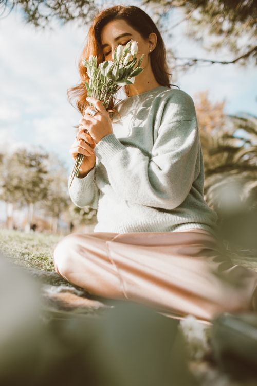 Free A woman sitting outdoors in a sunny park, admiring a bouquet of flowers with a serene expression. Stock Photo