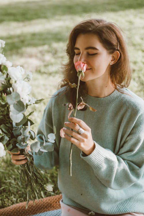 Woman in Sweater Smelling Pink Flower