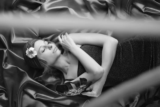 A peaceful woman with closed eyes lies on silky fabric, holding a feather, creating a serene and tranquil mood.