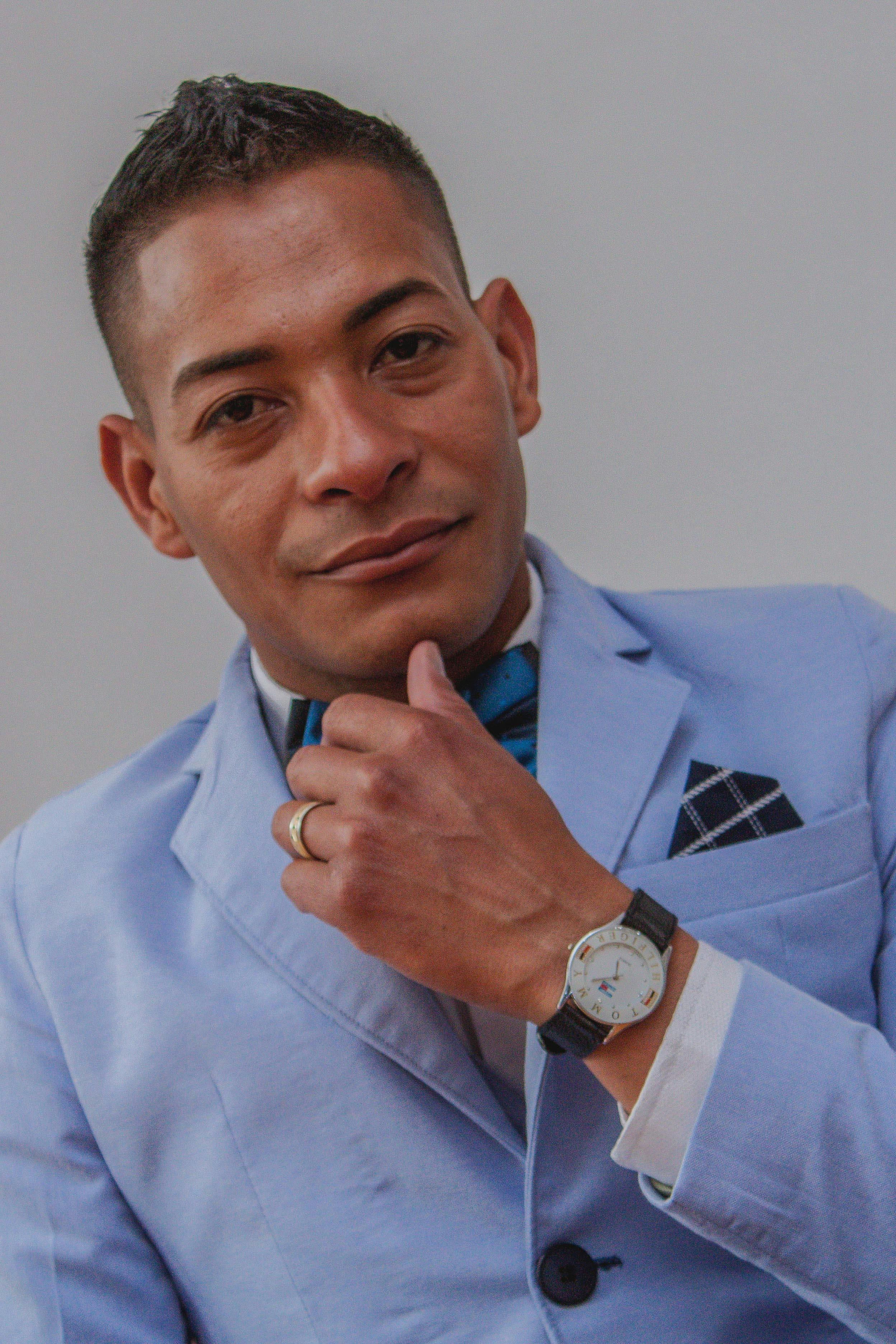 Portrait of a confident man in a light blue suit, wearing a watch, posing indoors.