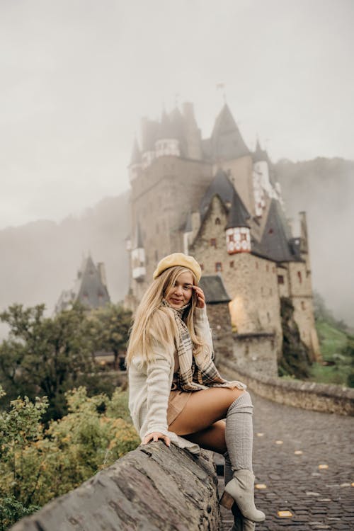 Free Woman Sitting on a Concrete Wall Near Eltz Tower while Smiling at the Camera Stock Photo