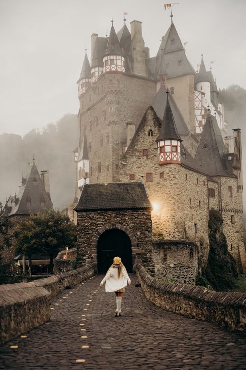 Free A woman walking towards the historic Eltz Castle on a foggy morning in Germany. Stock Photo
