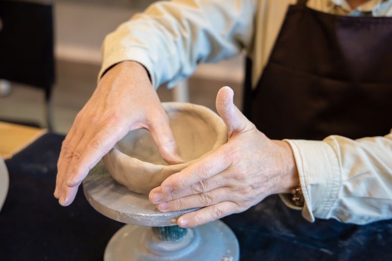 Hands shaping clay on pottery wheel