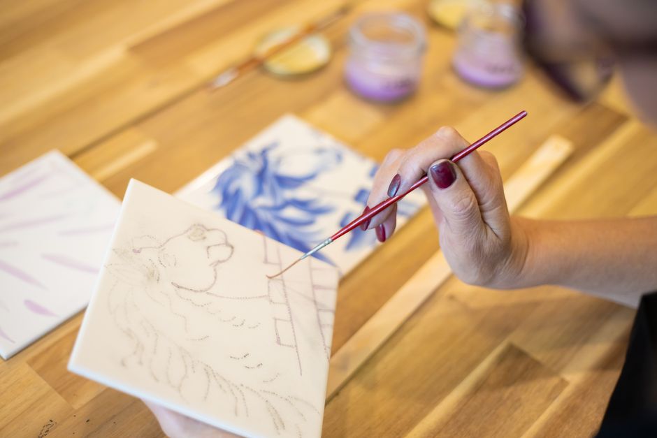 A detailed view of a hand painting a decorative pattern on a ceramic tile with a fine brush.